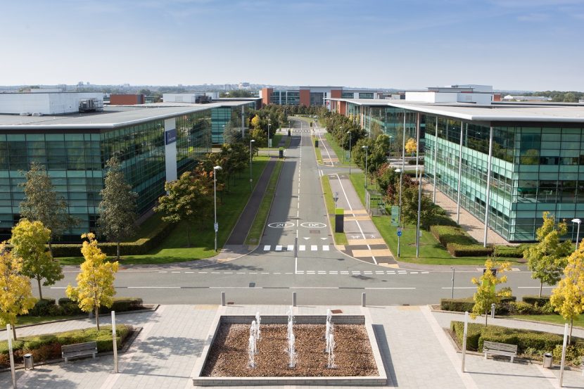 Long, straight road lined with trees and with large glass panelled office blocks on either side