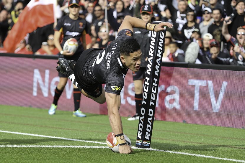 Man in full black rugby kit diving onto the try line with ball touching the ground