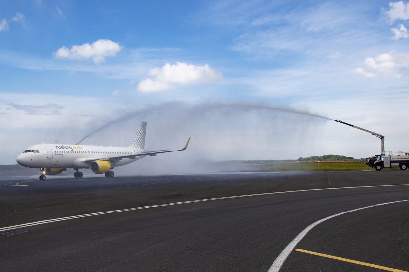 Airplane on runway with large water sprinklers on either side showering the plane as it comes in