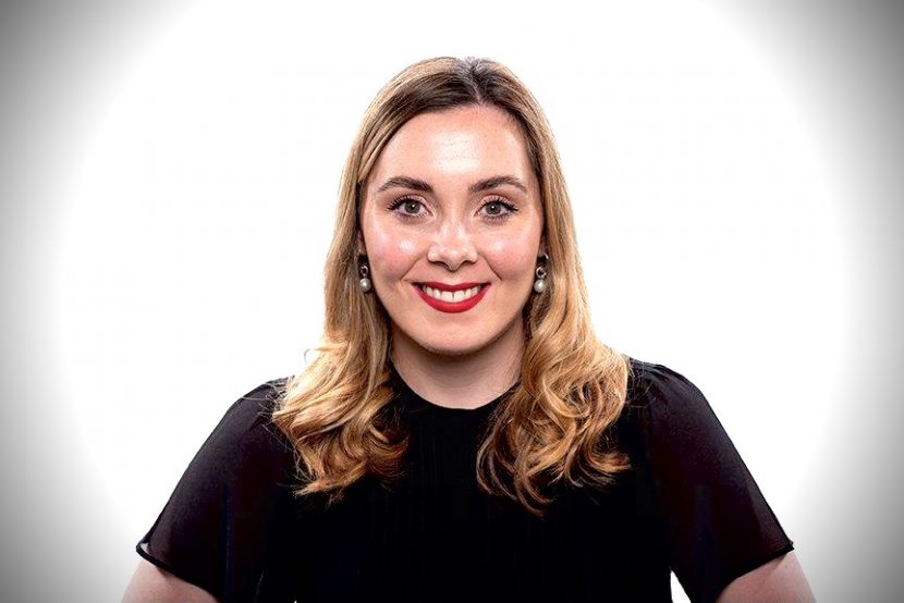 Headshot of Kirsty Russell smiling towards camera head on. Kirsty has shoulder length dark blonde hair, red lips and a short sleeve black top on.