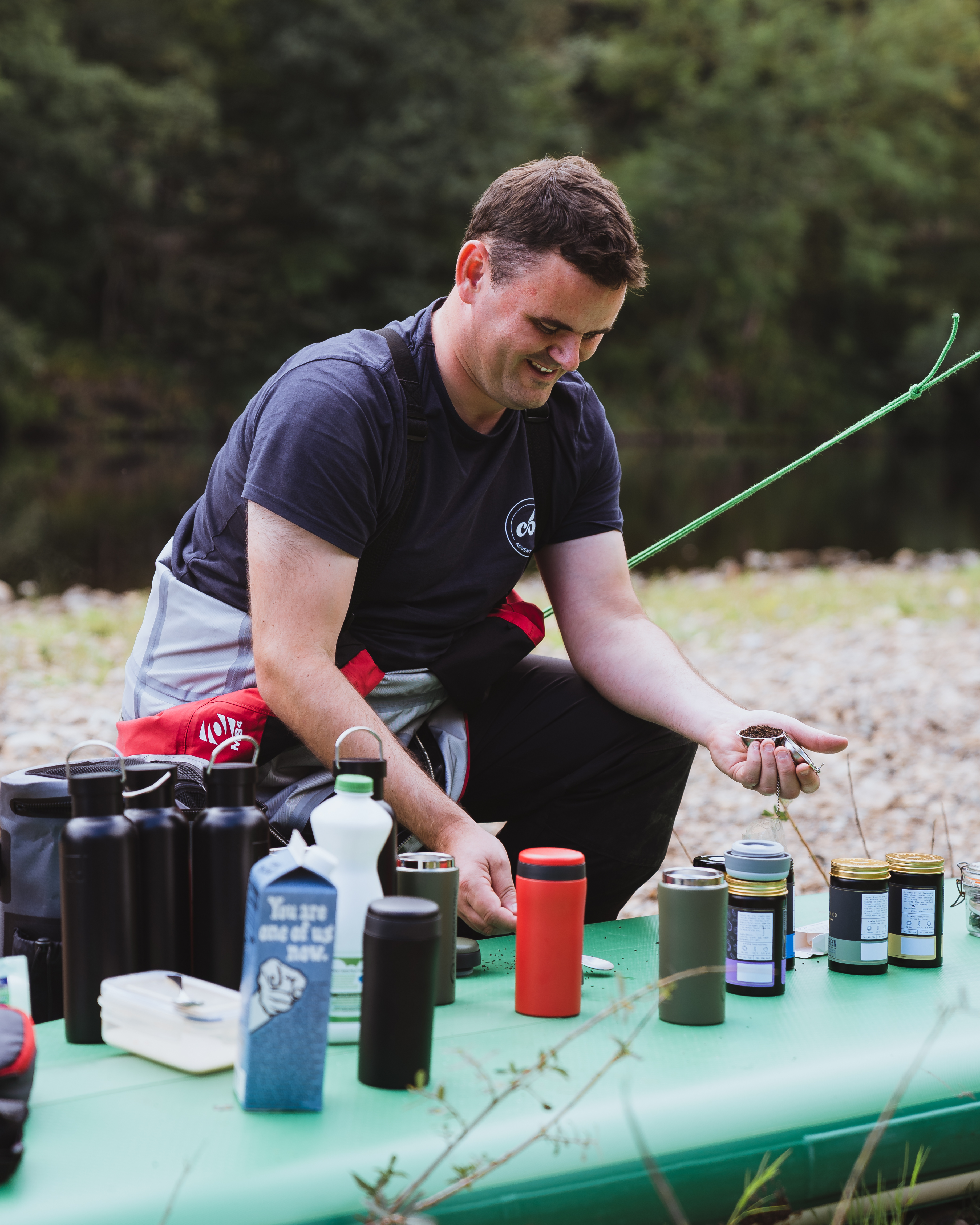 Man is crouched above a large mint green paddle board which has lots of jars and cans on top of it.