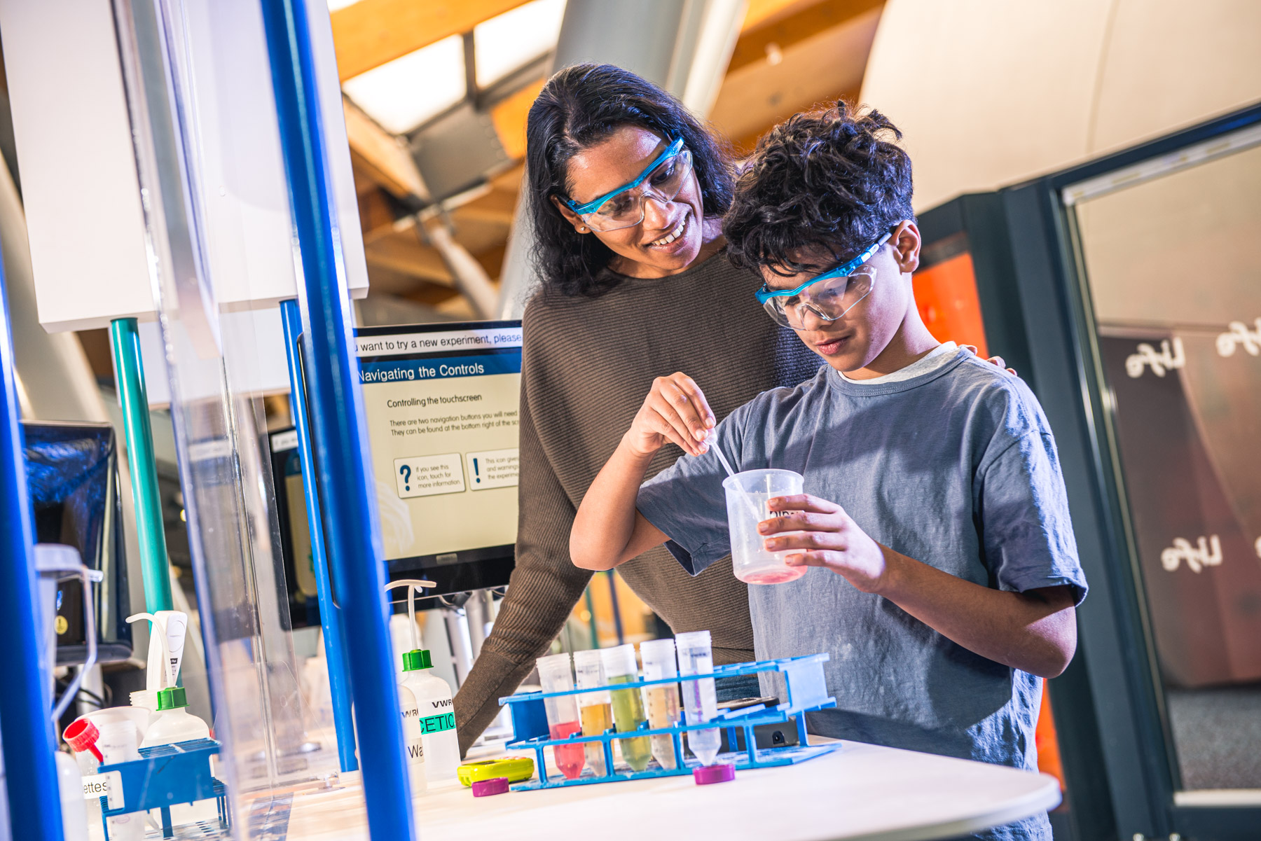 Child using pipette and wearing safety glasses in a laboratory with parent watching over them