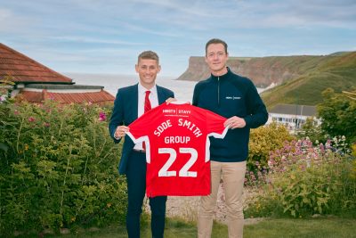 Two people stood holding red, branded football top between them