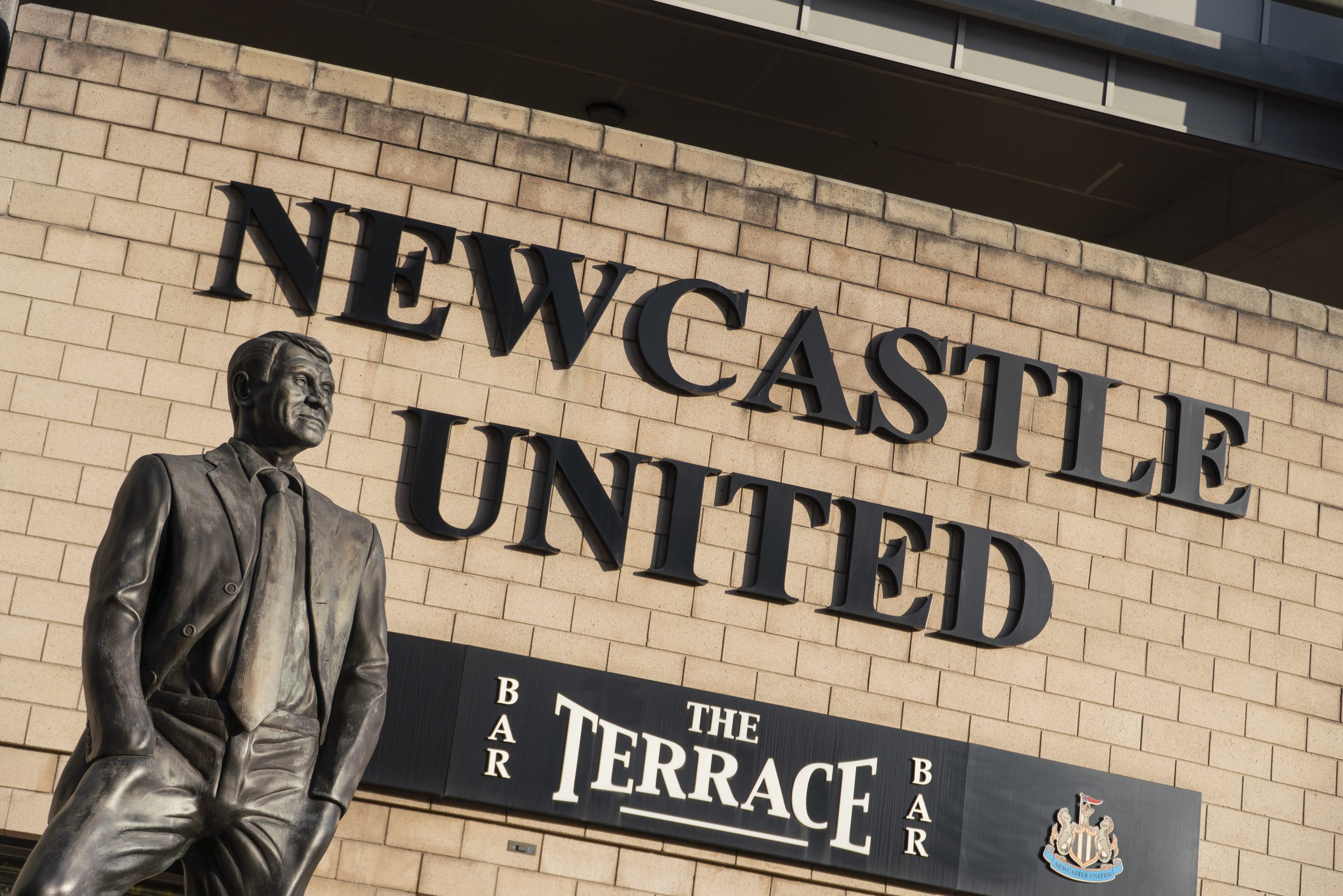Image of Newcastle United sign outside of the St James' Park stadium with statue of Sir Bobby Robson in the foreground