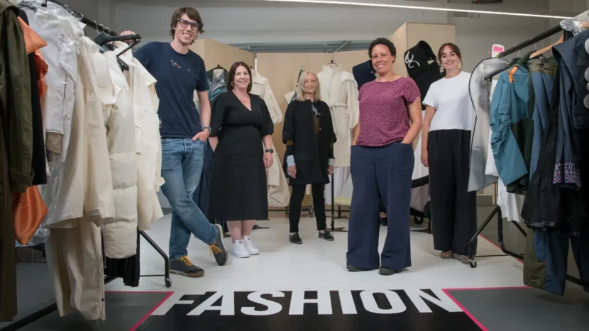 Image of five members of the project team stood in front of racks of clothing in a low-ceilinged room.