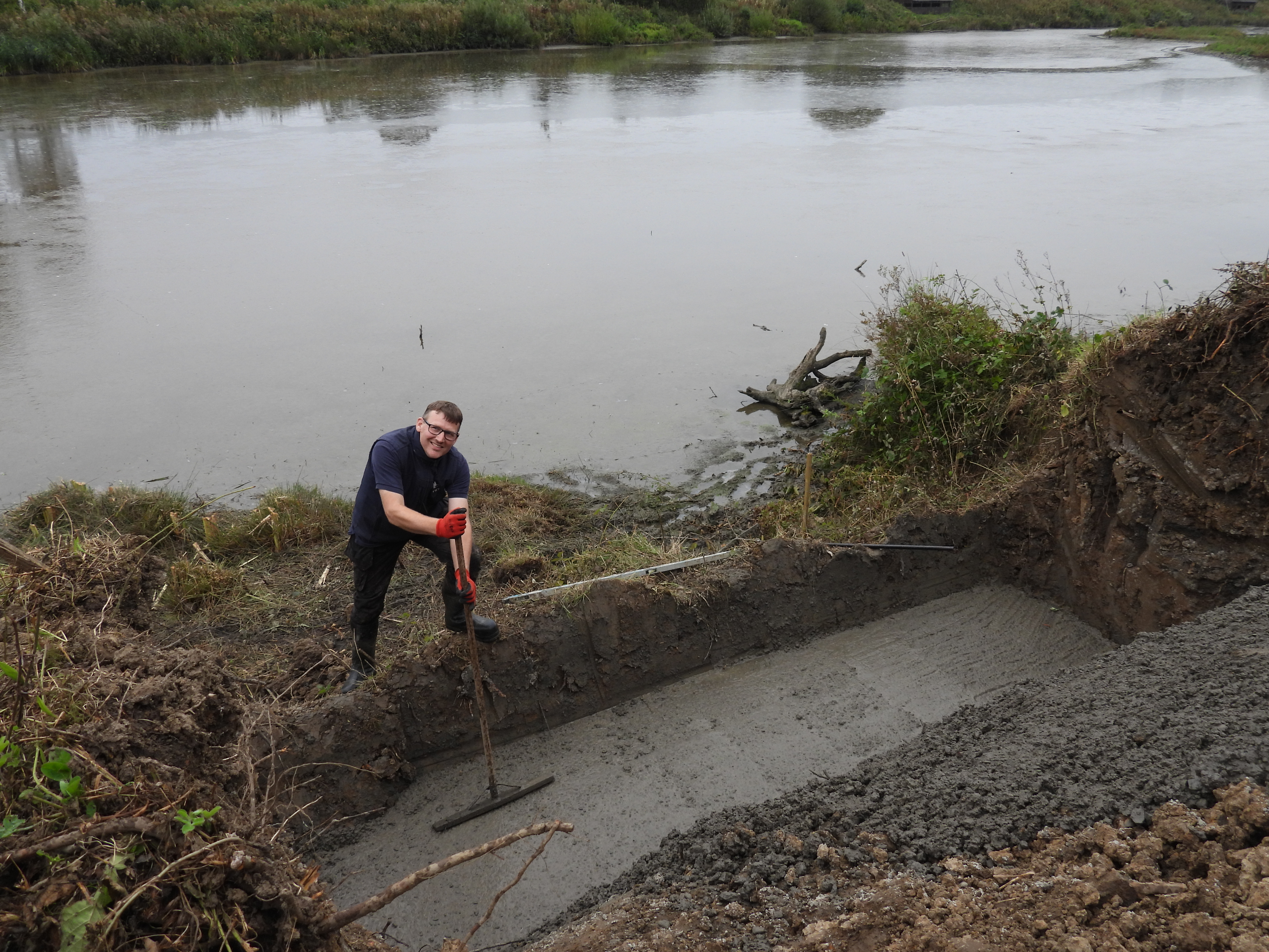 Reserve warden digging rectangular hole on the banks of a large pond or river.