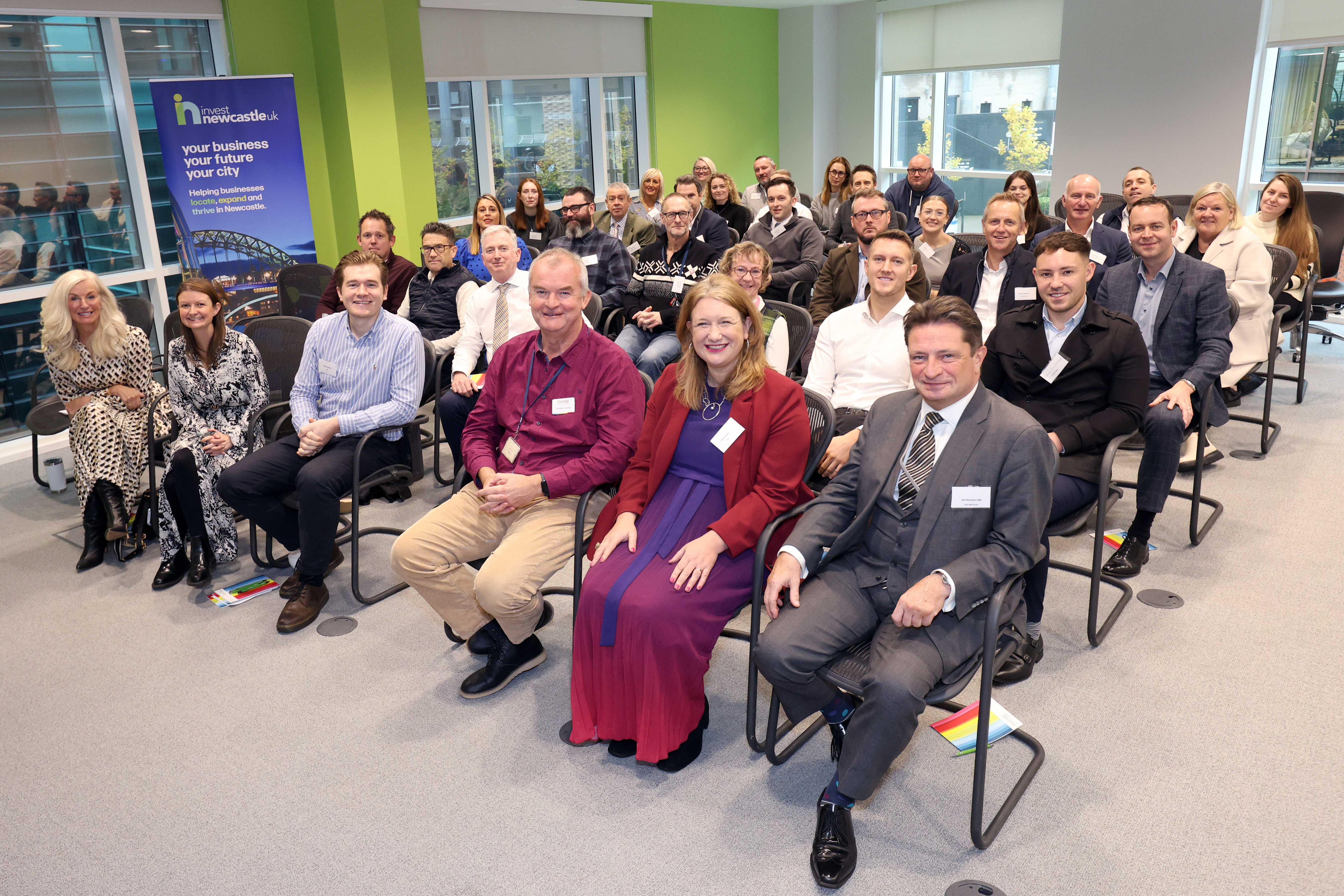 Large group of people sat in rows at event smiling towards camera