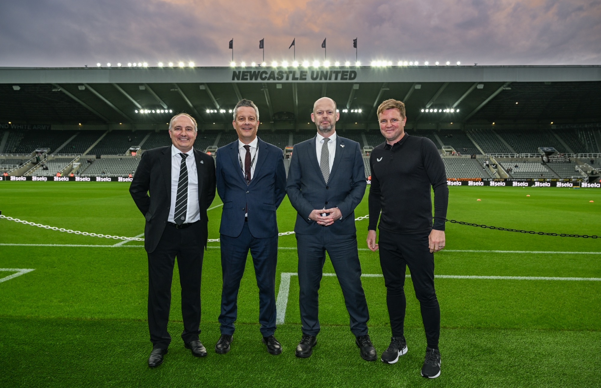 Four city leaders stood on pitch at St James' Park in suits and Eddie Howe in black NUFC training kit.