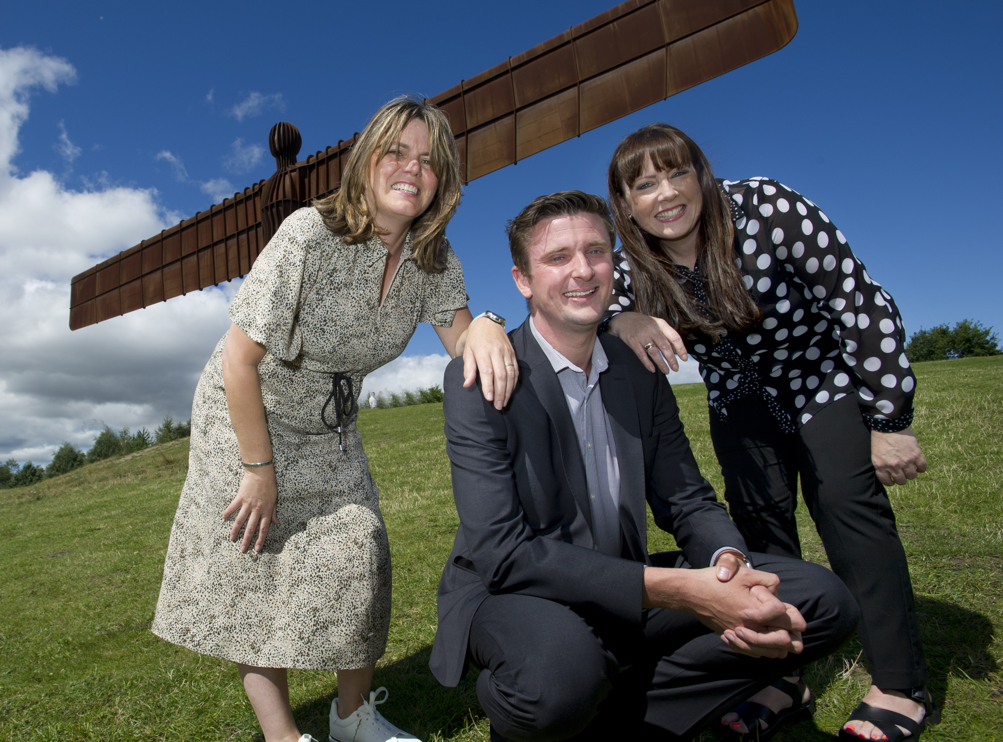 L- R: Sharon, David and Valerie smiling at the camera standing in front of the Angel of the North.