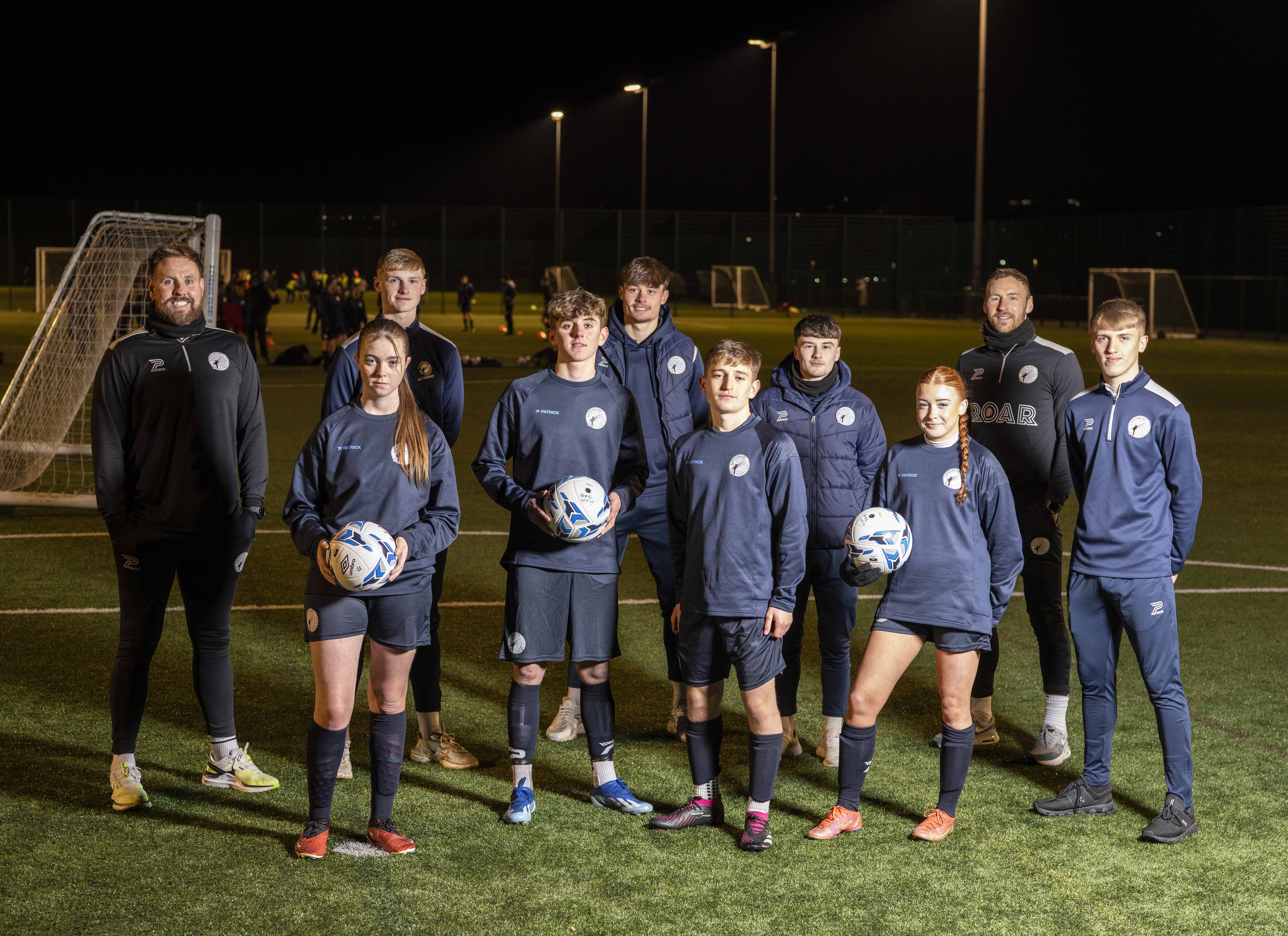 Gateshead FC staff and players from the first team and Academy with new Junior Academy players standing on a football pitch smiling at the camera.