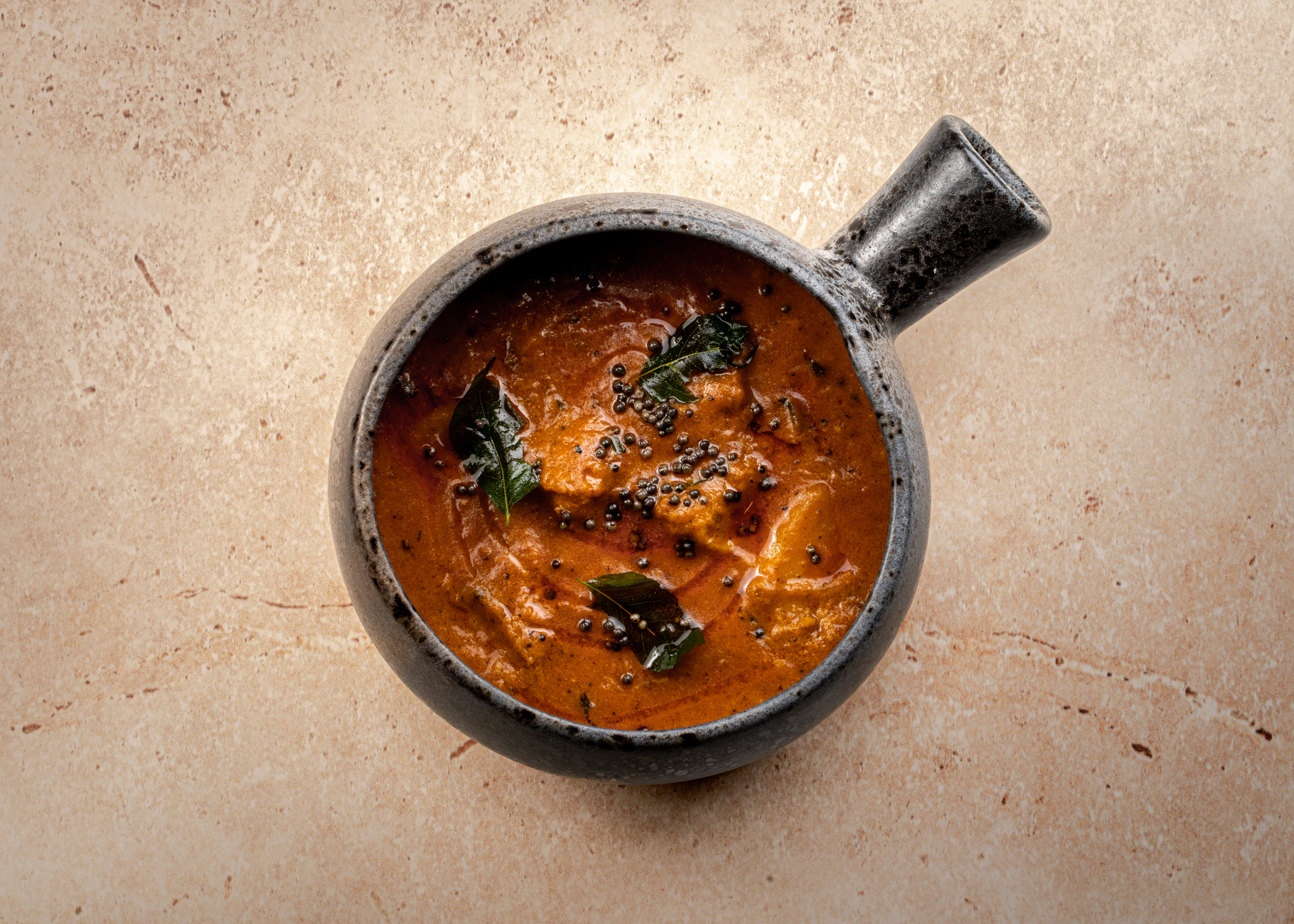 Birdseye shot of Dabbawal Railway Lamb Curry in a dark pot against a grey concrete surface.