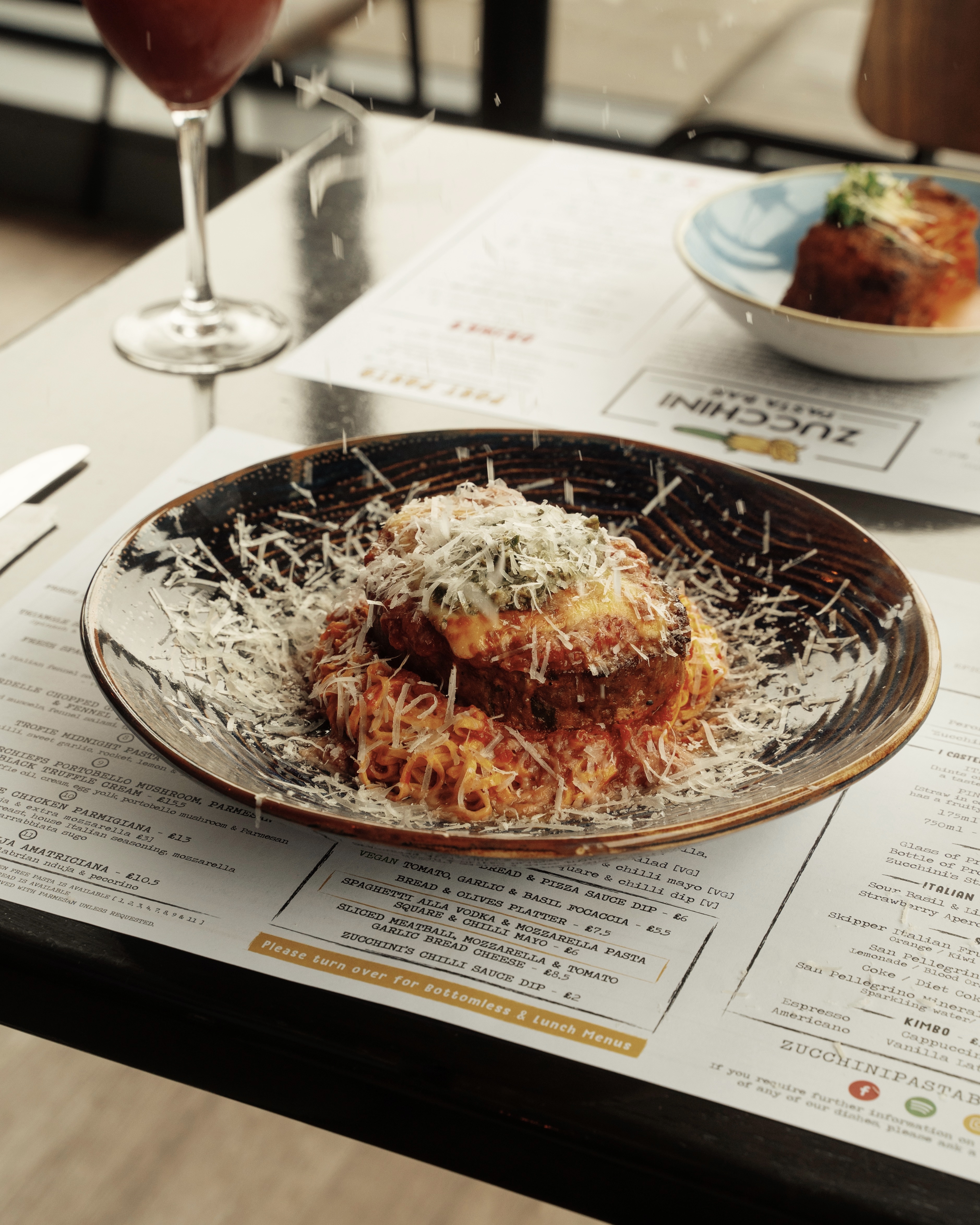 Image of a cheesy pasta dish in a large, shallow bowl on a table at Zucchini Pasta Bar