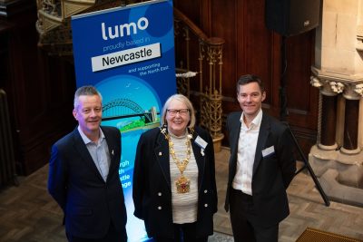 Newcastle City Council leader Cllr Nick Kemp, Lord Mayor of Newcastle Cllr Veronica Dunn, and another person stood in front of Lumo banner smiling to camera.