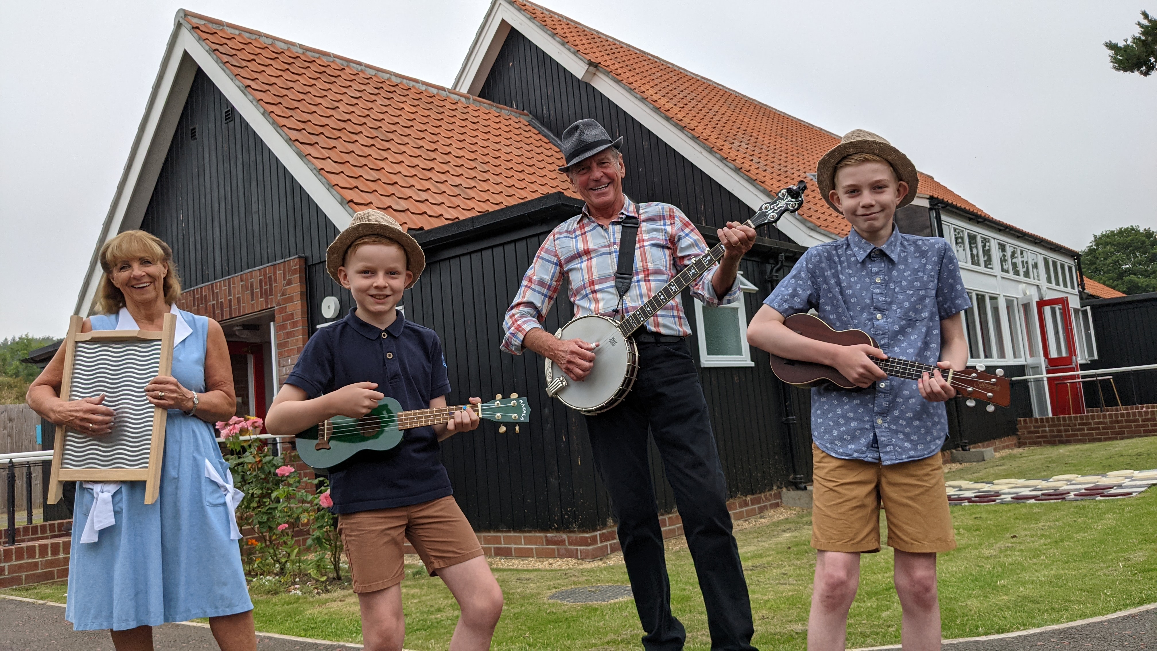 Group of children and adults playing ukuleles and banjos outside of the Beamish Community Hall