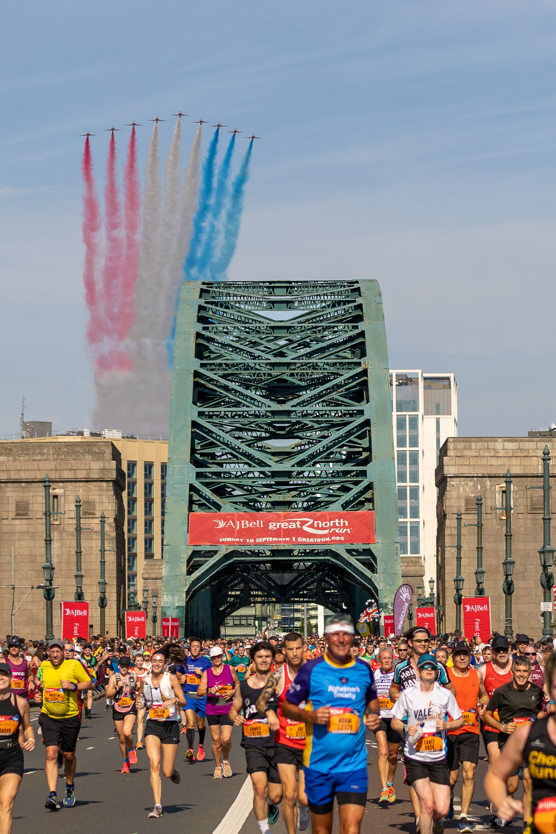 Image of the Red Arrows planes flying over the Tyne Bridge as runners of the Great North Run run across.