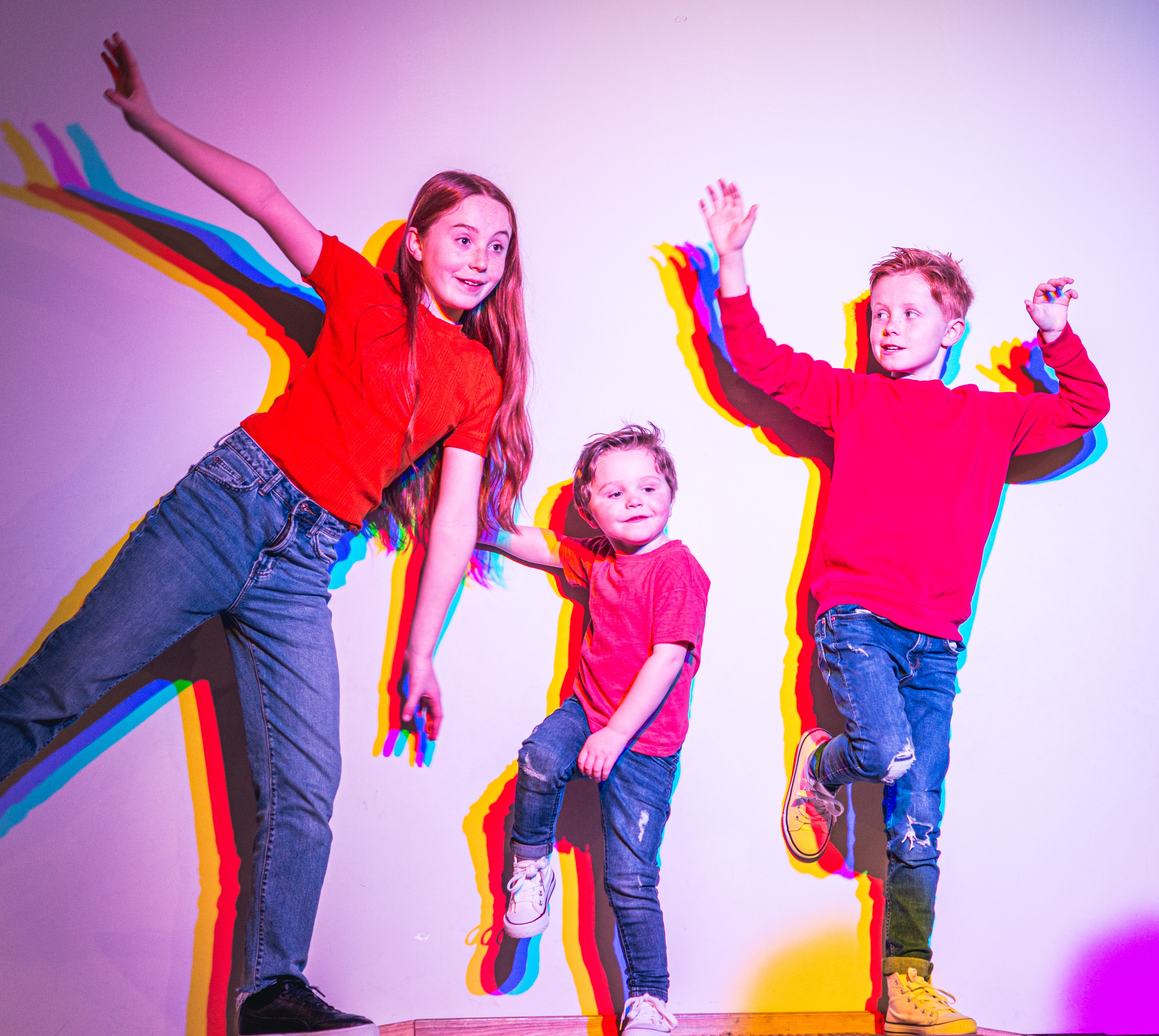 Group of three children stood against a plain white backdrop posing in varying positions