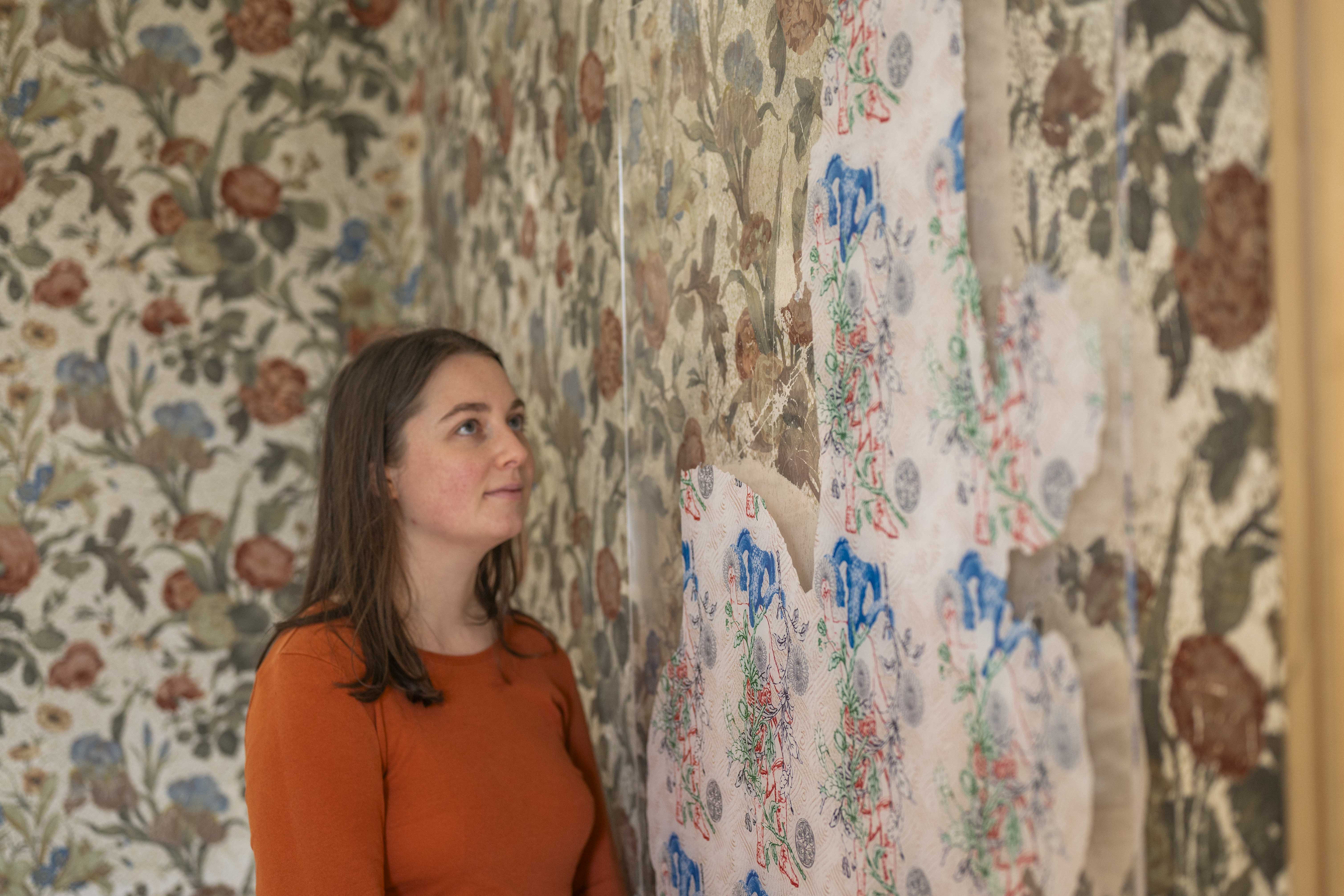 Woman in a room looking towards patterned wallpaper