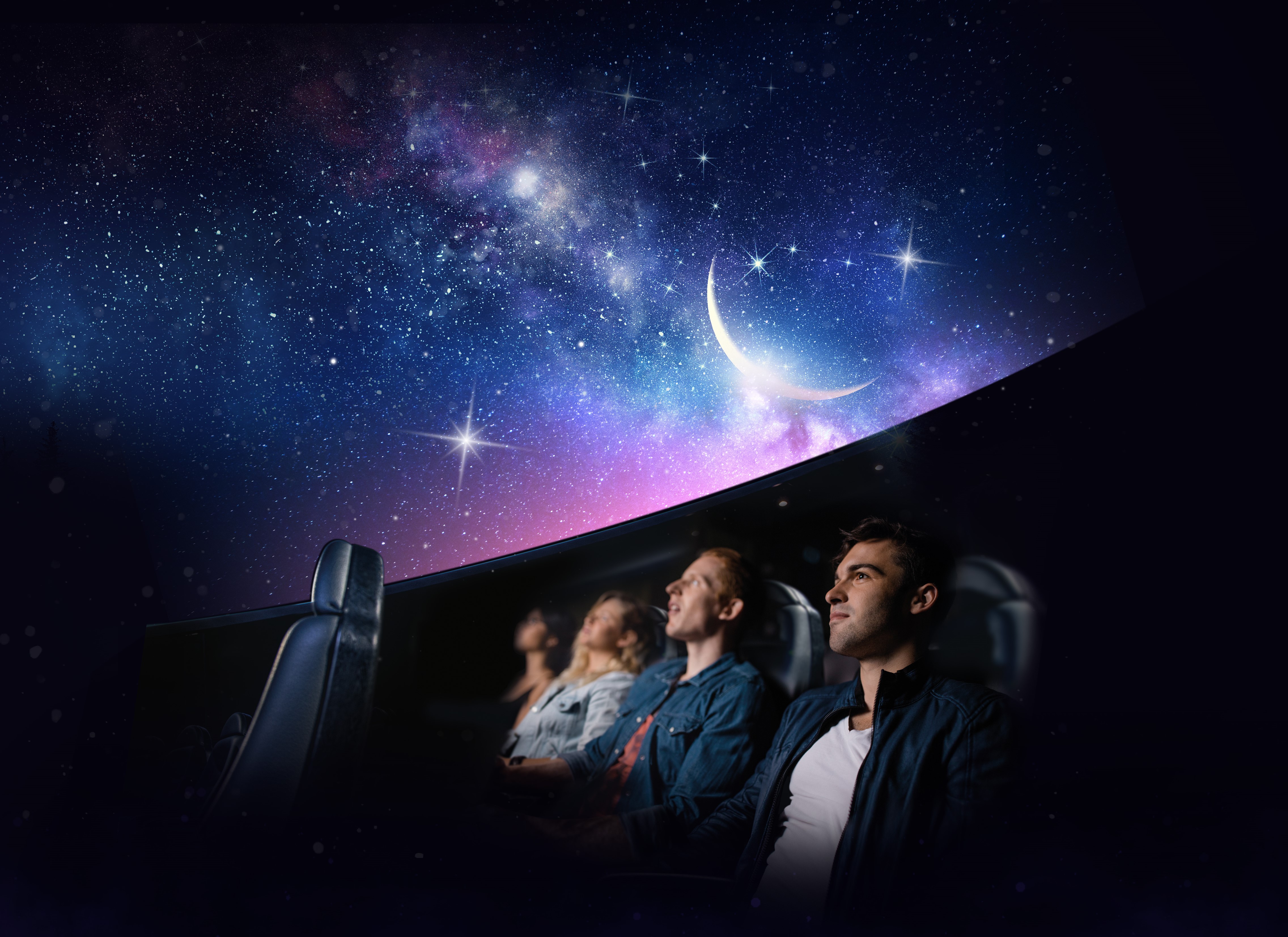 Three people sat in a row looking up to a night sky/space at a planetarium