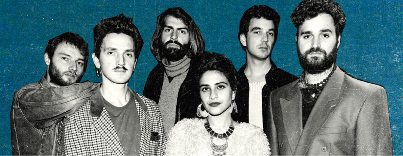 Group of six musicians stood in front of blue background looking towards the camera.