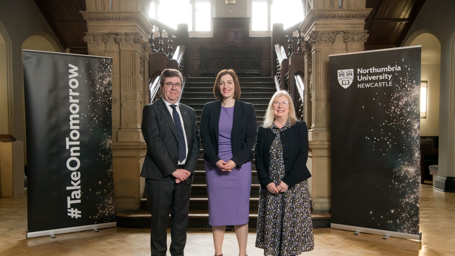 Professor Andy Long, Bridget Phillipson and Dr Roberta Blackman-Woods stood in front of old staircase with Northumbria University banners flanking either side.