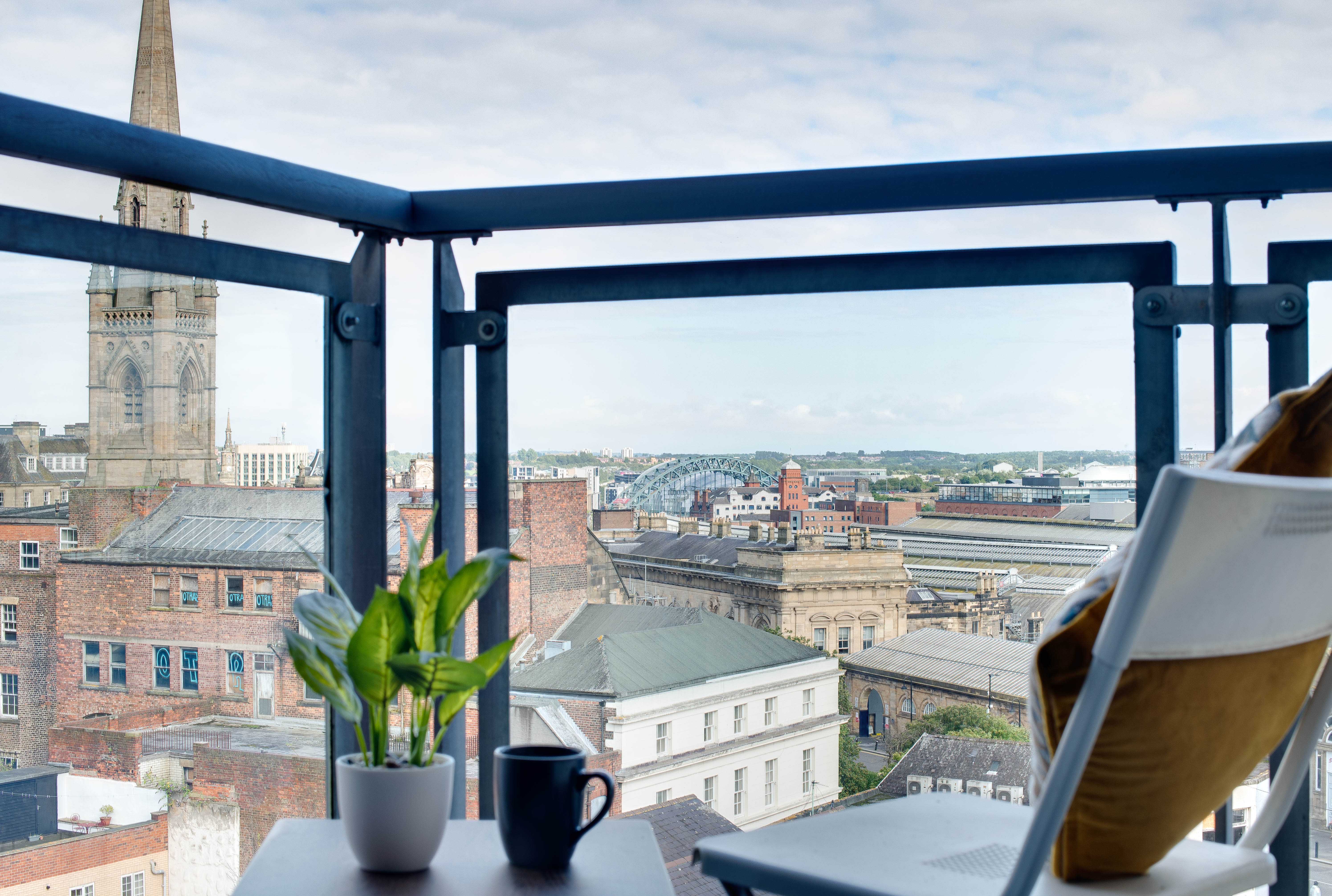 A shot of the Newcastle skyline from a glass-panelled balcony with a chair and side table in the foreground.