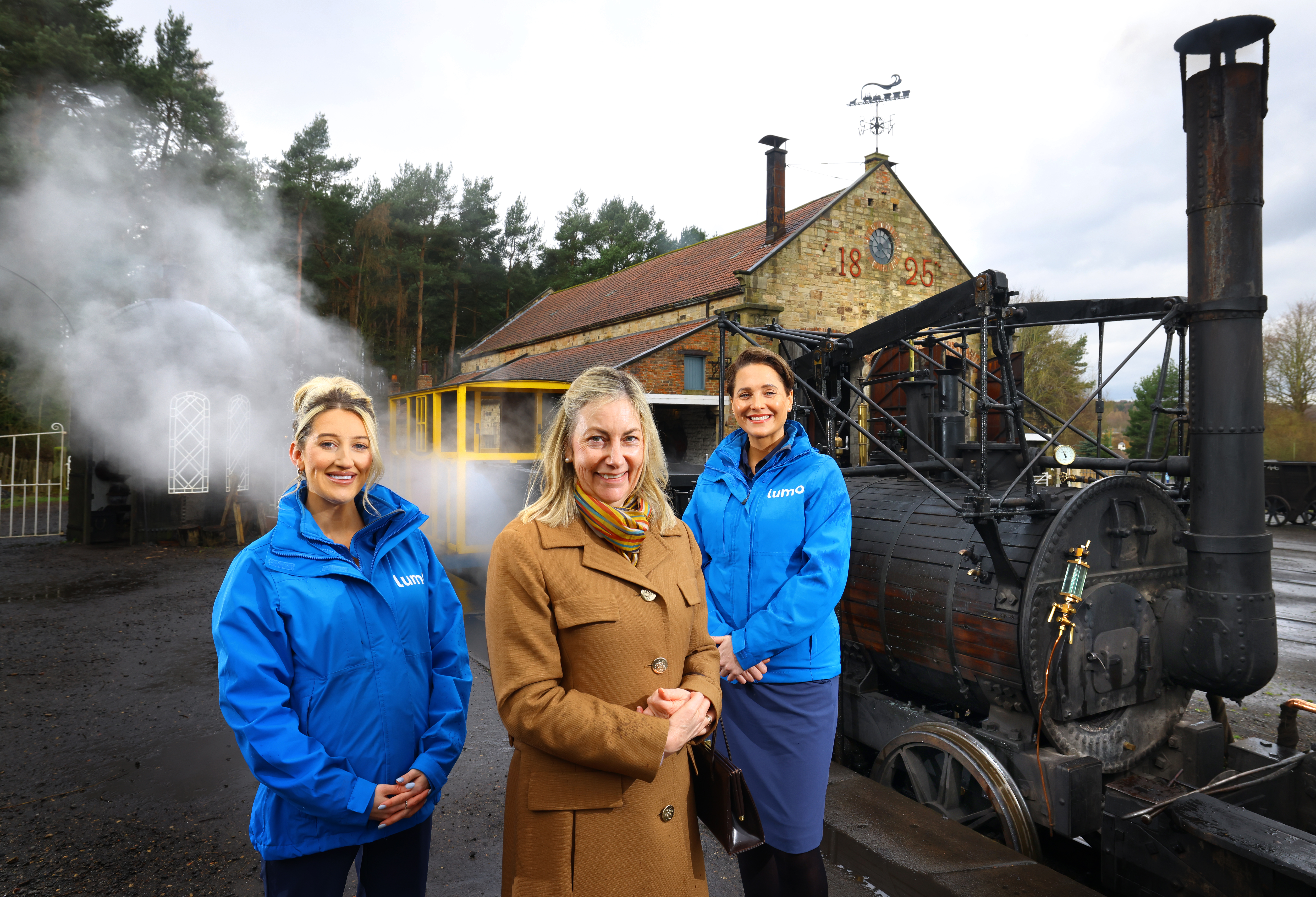 Image of two Lumo staff in their blue jackets with Liz Peart from Beamish in front of steam train at Beamish Museum