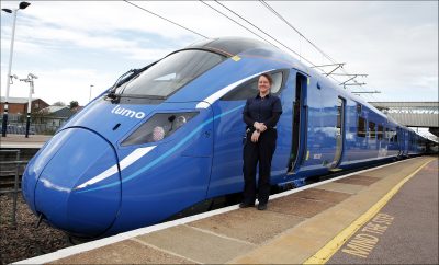 Carrie stood on a train platform next to the front of a Lumo train smiling to camera.