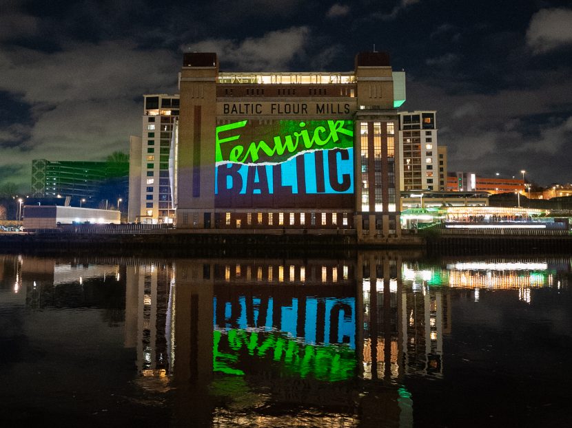 Side view of the Baltic gallery by the River Tyne with the Fenwick and Baltic logos projected on the side of the building.