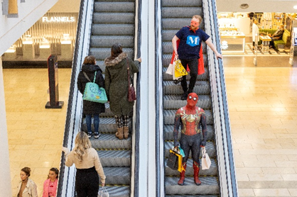 Shoppers on an escalator one is dressed in a Spiderman costume.