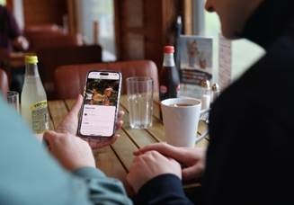 Over the shoulder shot of two people looking at a mobile phone at a cafe table