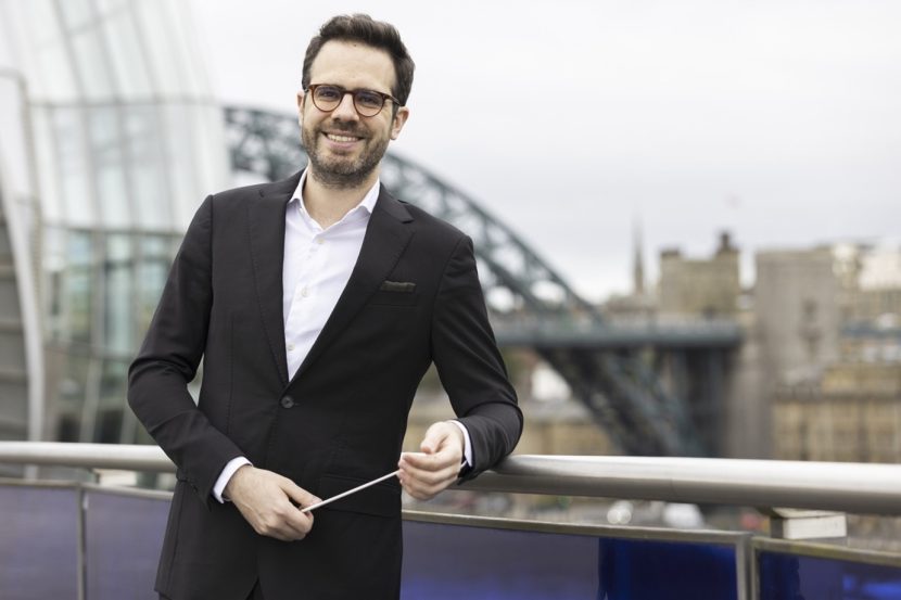 Conductor stood outside The Glasshouse with the Tyne Bridge in the background smiling to camera.