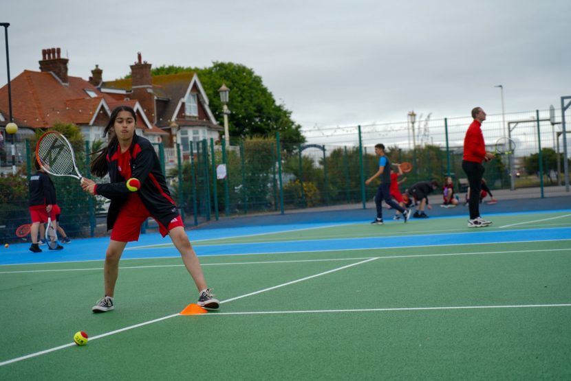 Image of child playing tennis on a brightly coloured tennis court