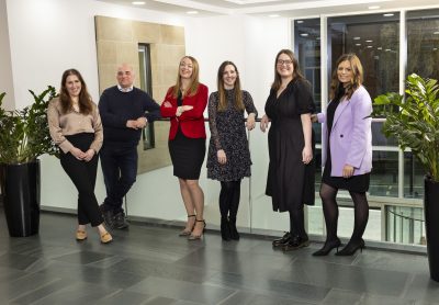 Group of Muckle employees stood near reception desk smiling to camera.