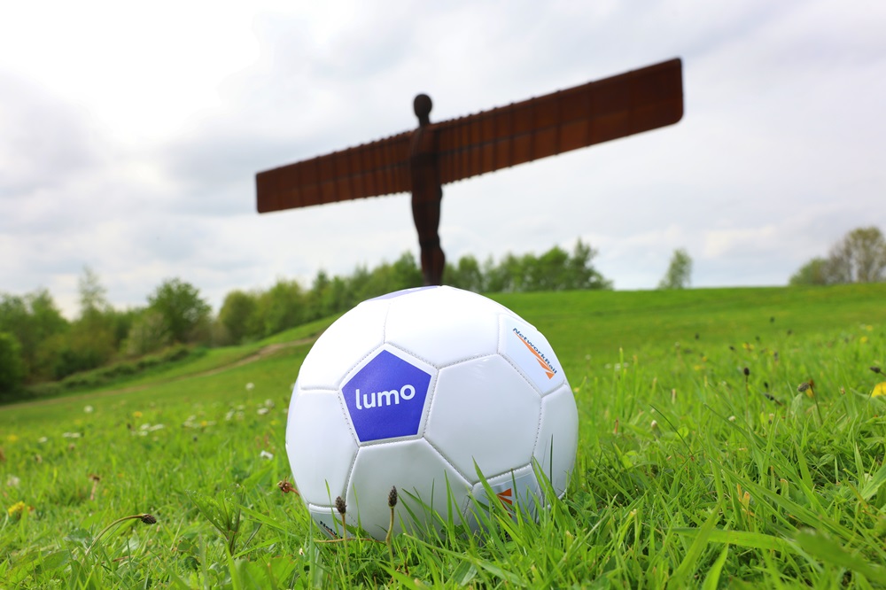 Lumo and Network Rail branded football on grass with Angel of the North in the background.