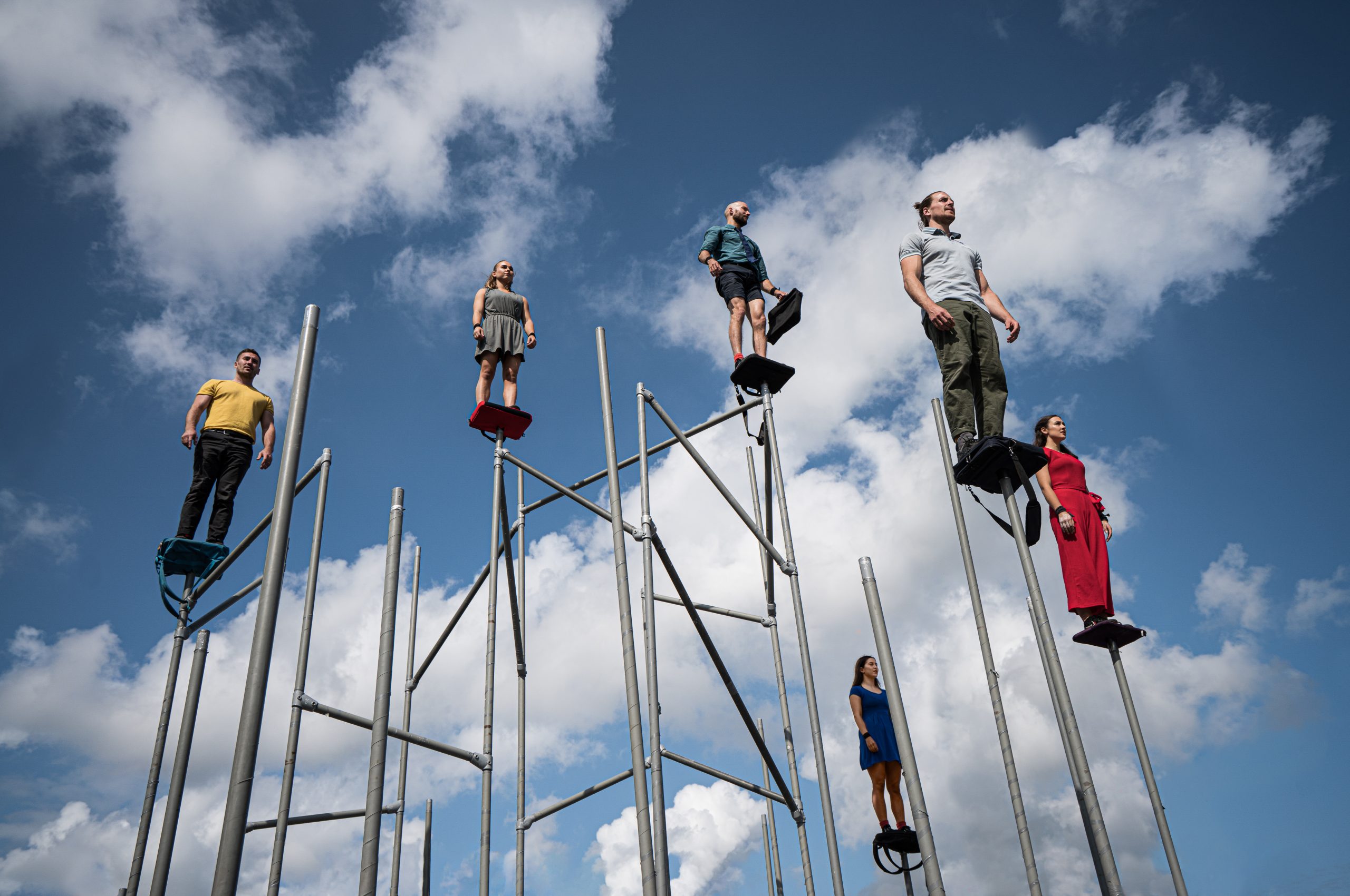 Image of people stood on top of large poles with a blue sky in the background