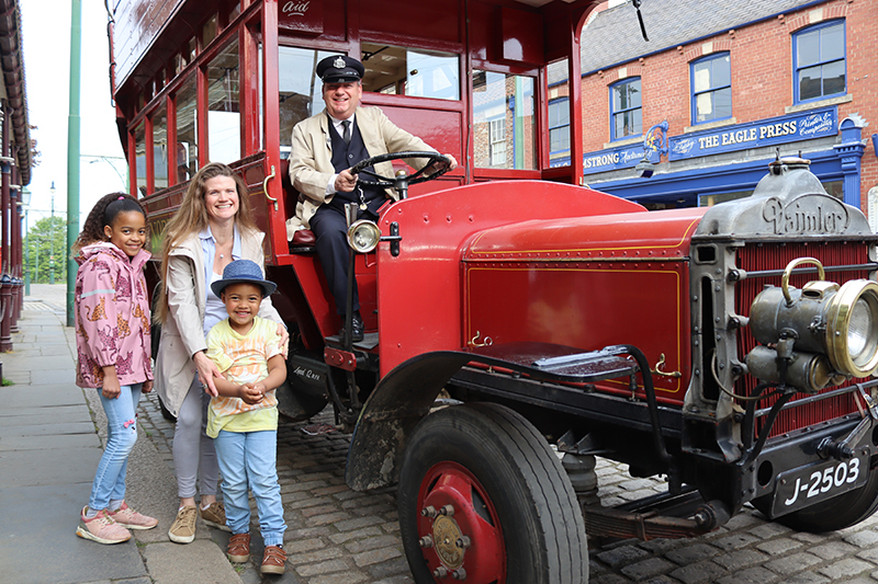 Adult and two children stood beside a retro bus smiling to camera with bus driver grinning beside them.