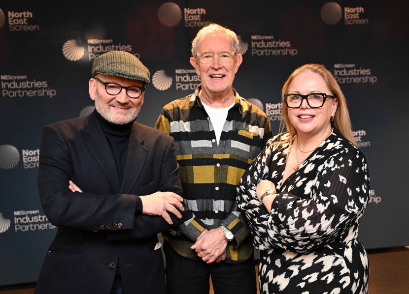 Three people stood closely together smiling to camera.