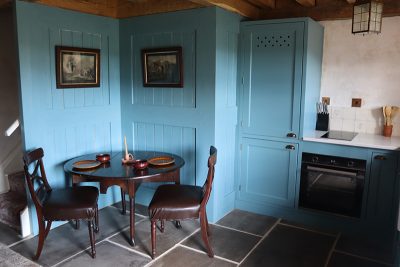Small nook in one of the cottages at Beamish Museum. A small wooden table and chairs are in front of the light blue wood-panel wall.