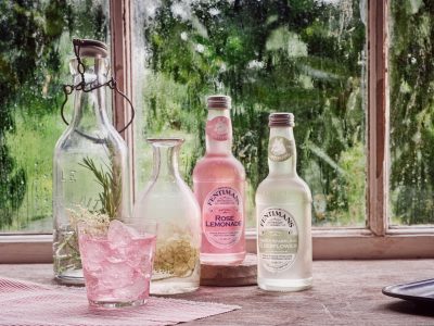 Fentimans bottles and a glass of pink lemonade on a table in front of a window.