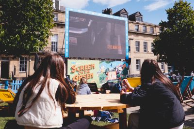 People sat on a picnic table looking up at the 'Screen on the Green' in the sunshine