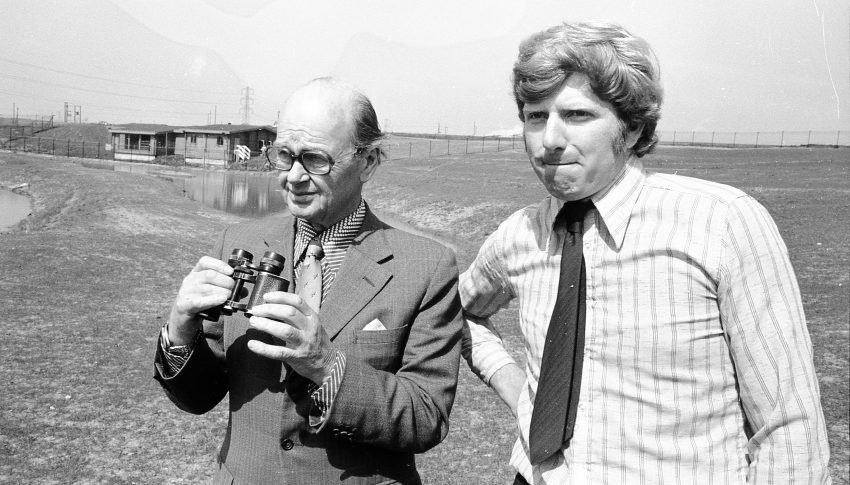 Black and white photo from 1975 of Peter Scott holding binoculars and stood next to John Secrett at Washington Wildlife Refuge