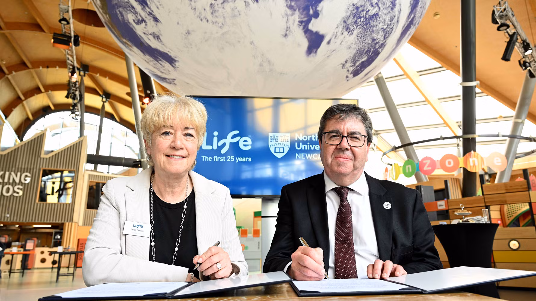 Linda and Andy sat together signing a document inside the Centre for Life.
