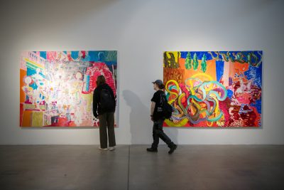 Two people looking at two pieces of large art on a white wall.