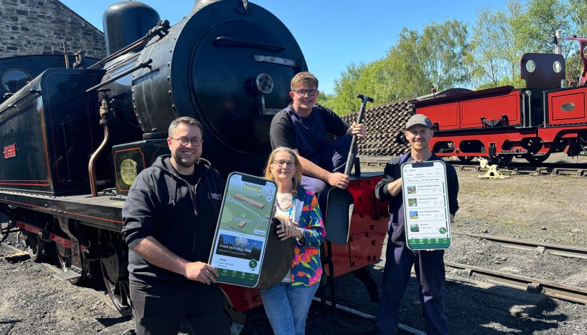 Four people stood by a steam train holding cardboard cutouts of a mobile phone