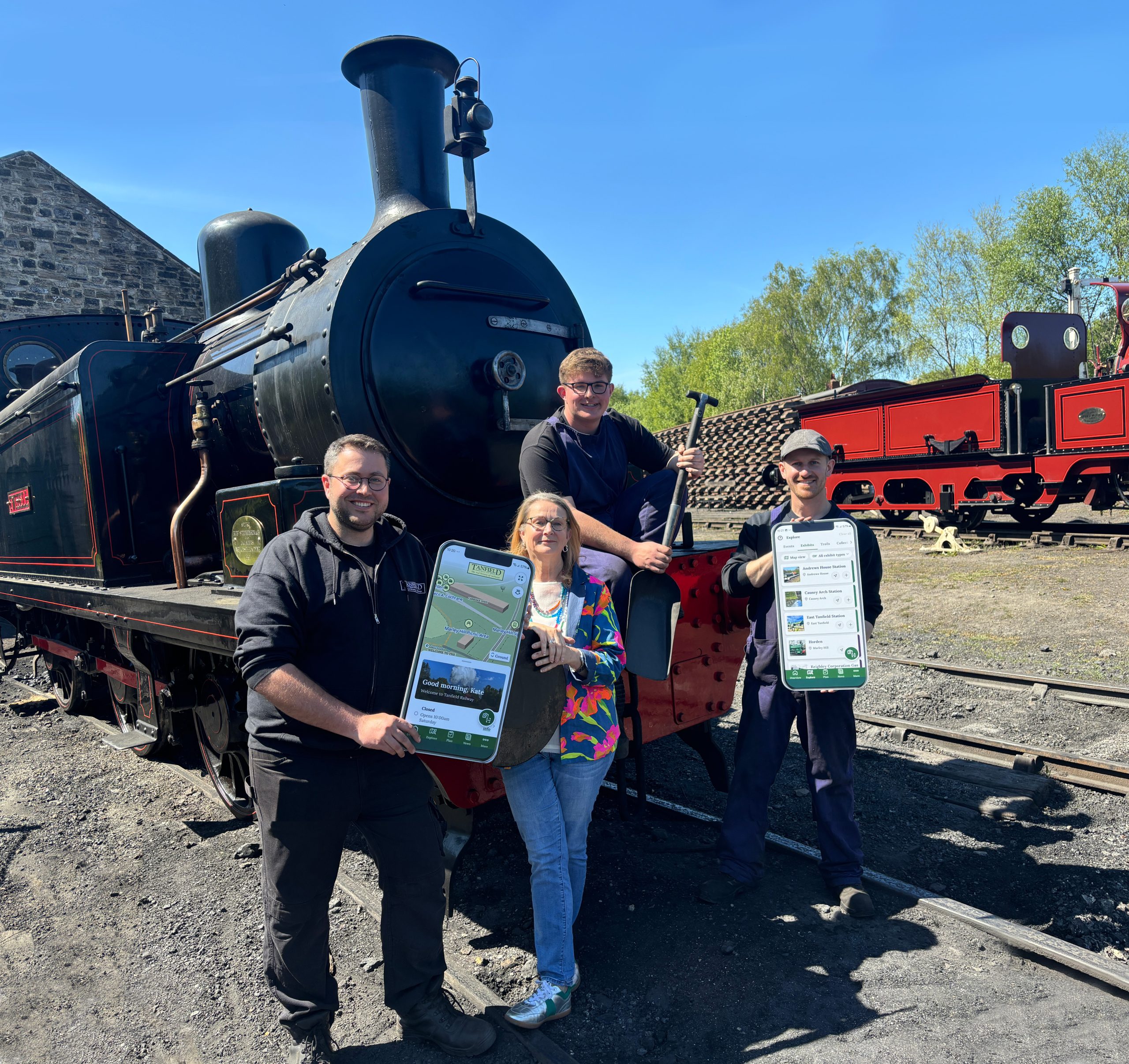 Four people stood by a steam train holding cardboard cutouts of a mobile phone