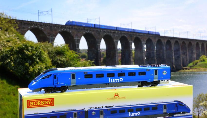 Lumo train model on top of its box underneath a rail bridge which has a real-life Lumo train crossing.