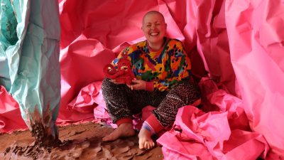 Person sat within an art installation smiling widely to camera.