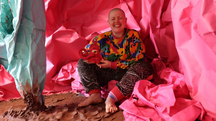 Person sat within an art installation smiling widely to camera.
