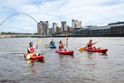 Four people in kayaks on the River Tyne with the Millennium Bridge in the background