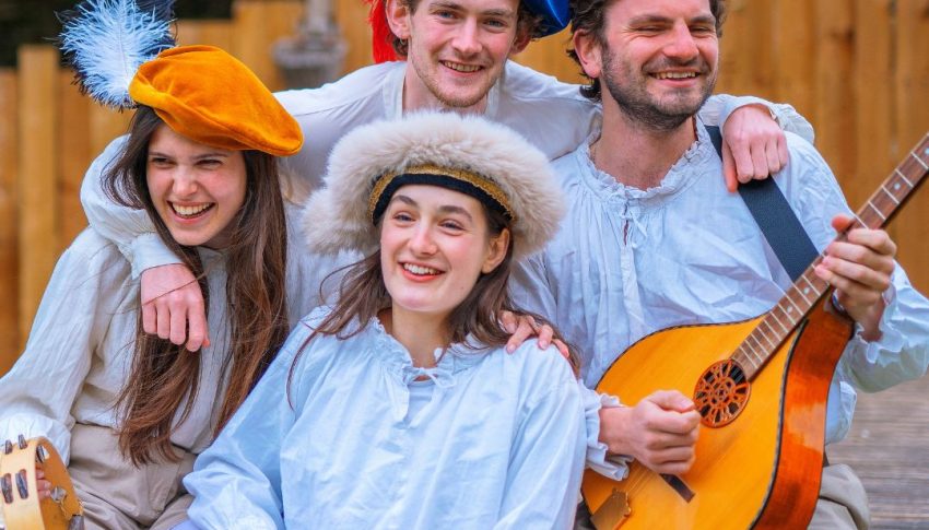 Four people holding medieval instruments and wearing medieval costumes smiling together as a group
